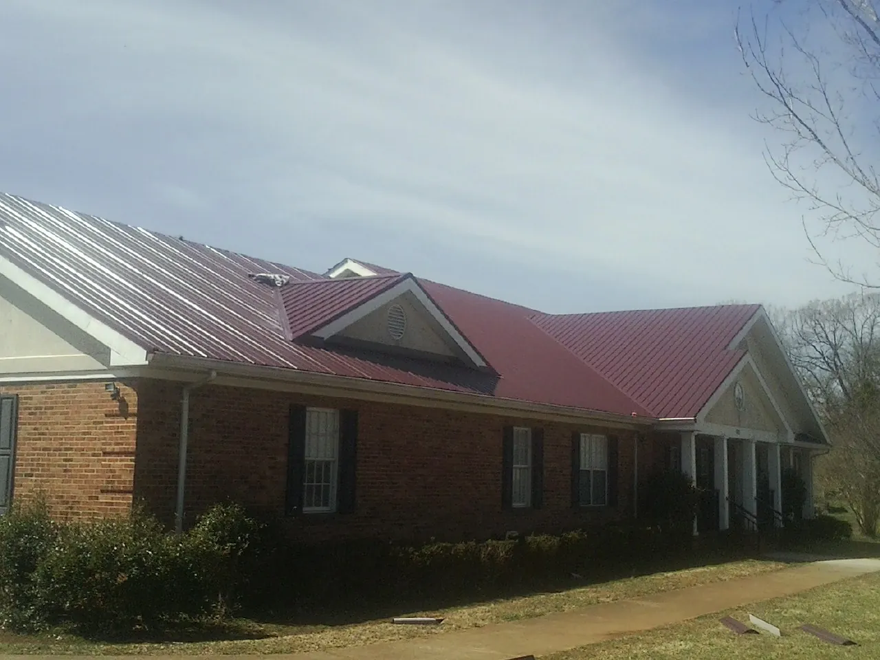 Red metal roof with gabled entries on a long brick building, from a Hail Damage Roof Repair job in Lillian
