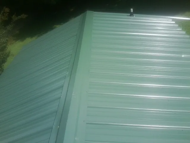 New green metal panels meeting at the ridge of a roof — Flat Roof Repair work by our crew in Lillian