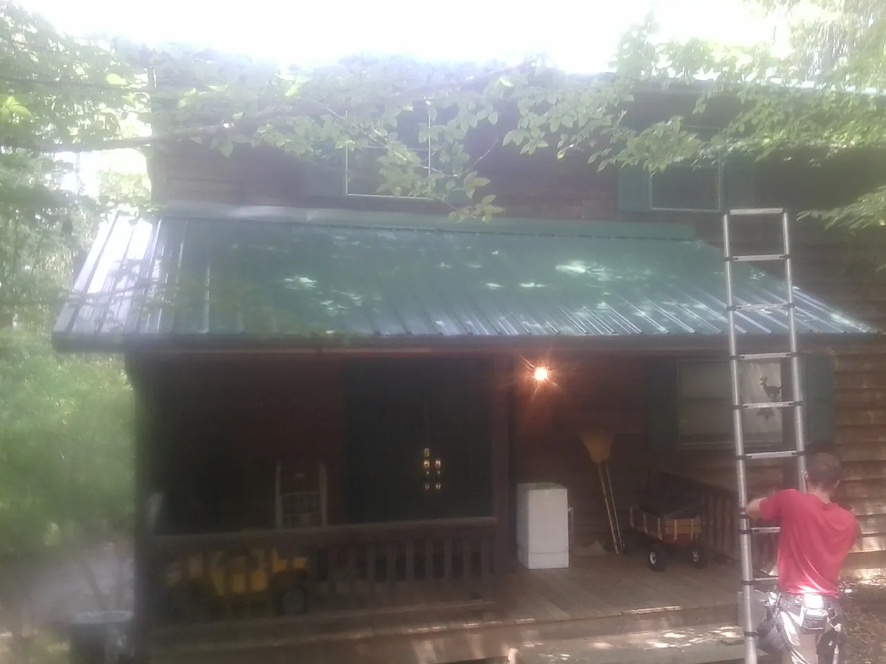 Worker on a ladder at the green porch roof of a wooded cabin in Lillian