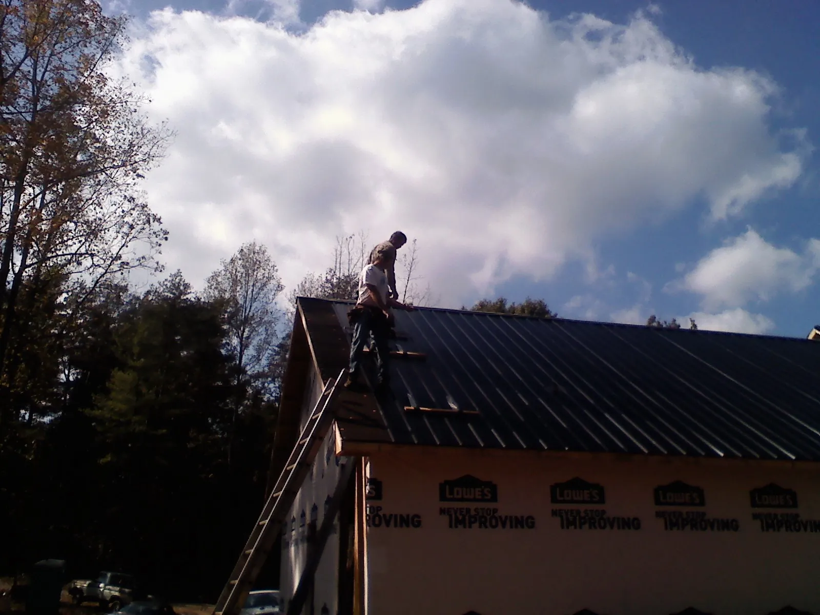 Roofer fastening dark metal panels high against a cloudy sky, from a Roof Inspection job in Lillian