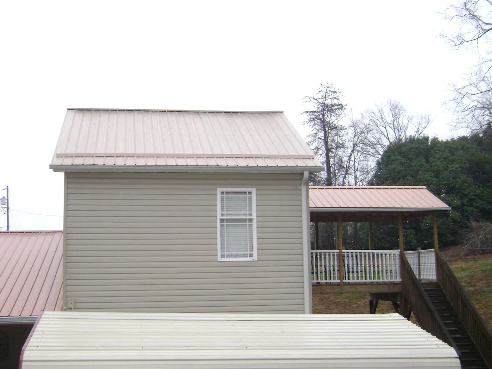 Tan metal roofs on a two story addition and attached porch, from a Roof Replacement job in Lillian
